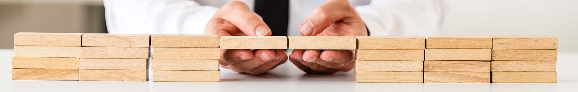 Wide view image of businessman making a connection between two stack of wooden pegs in a conceptual image of business solution or merger.