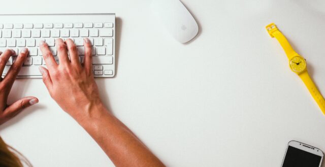 Hands typing on a keyboard placed on a desk