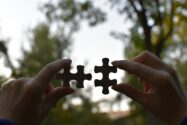 Two hands holding a puzzle piece in each, reaching to each other to complete the puzzle.