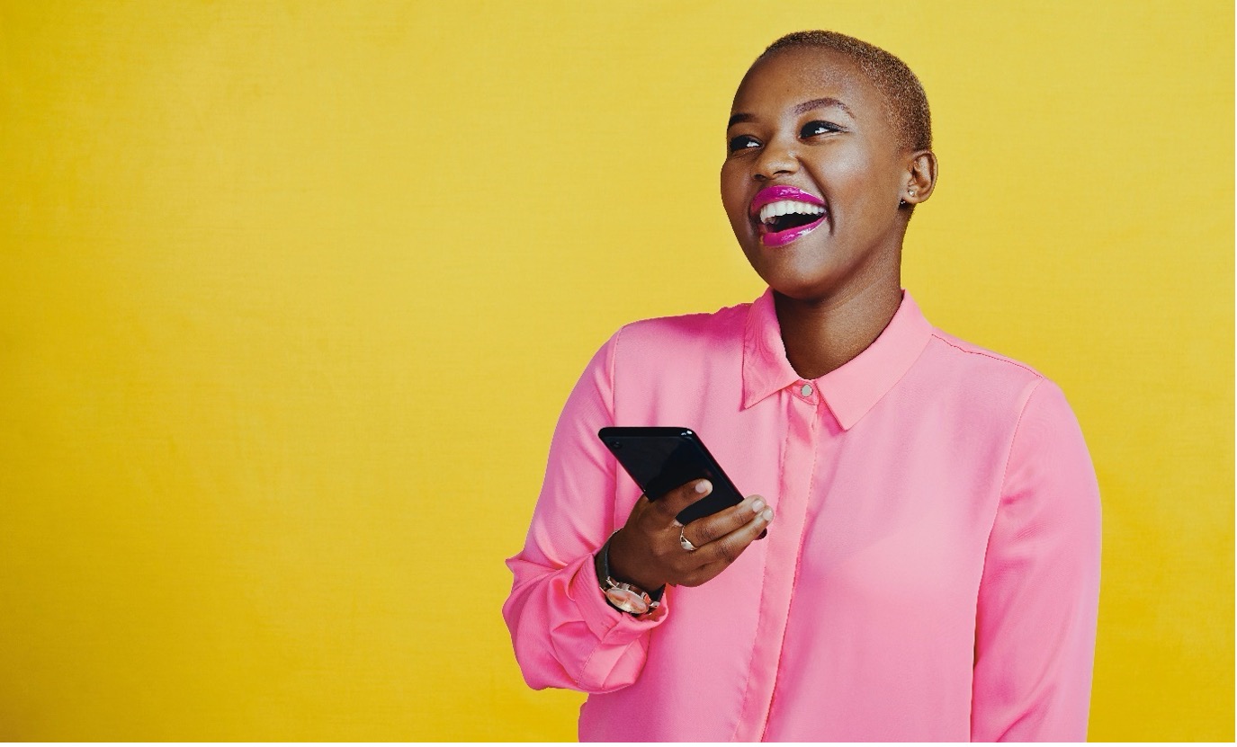 Young female person with short hair laughing while carrying a mobile in her right hand