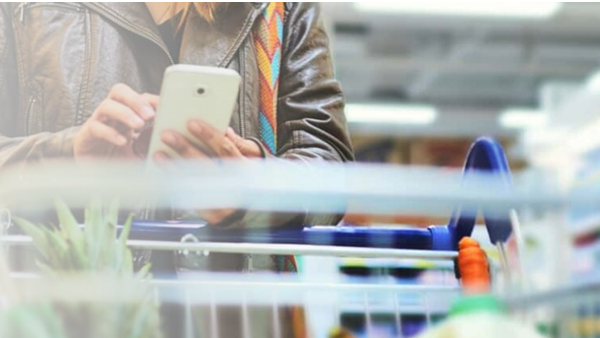 The silhouette of a female person typing on her mobile while shopping in a supermarket