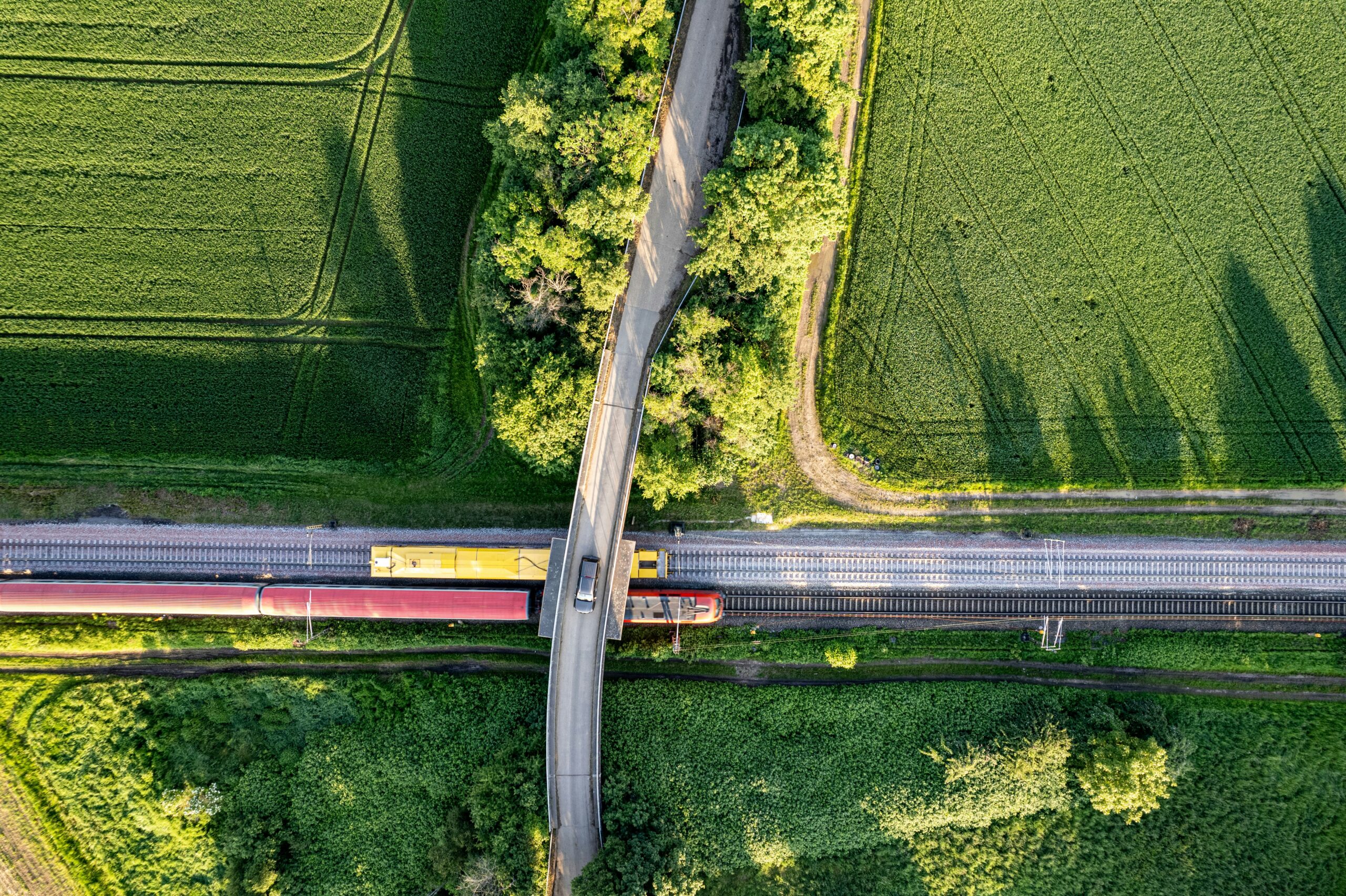 This aerial image captures a dynamic scene where agricultural greenery intersects with human infrastructure. It shows a train crossing a bridge over railway tracks that cut through vibrant green fields | SIOS Technology solution for disaster recovery and HA in Linux integration for SAP and AWS