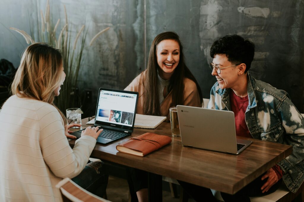 three women using computers and laughing while talking