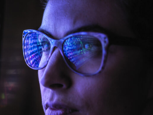 Female analyst with computer screen reflected in eyeglasses.