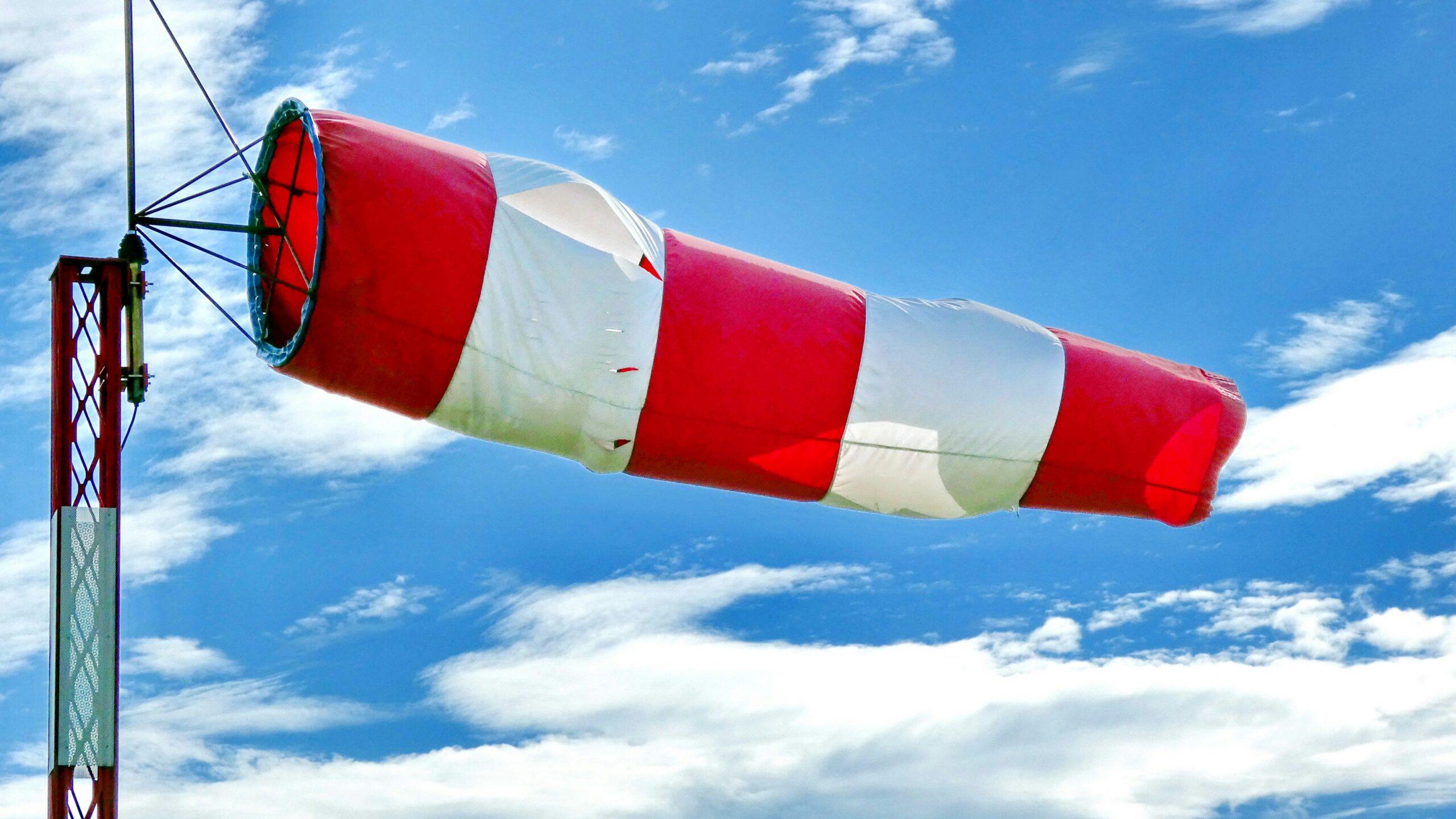 Red and white windsock extended in strong wind against a blue sky.