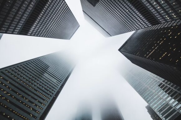 Looking up at tall office buildings in fog, representing executive accountability and enterprise pricing control.