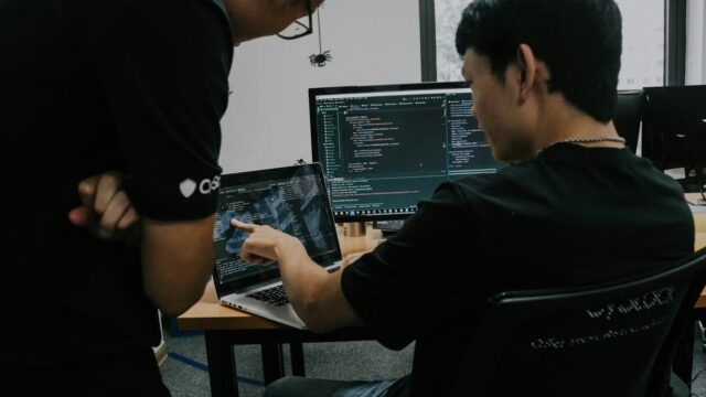 Two people working at computers in a dim office, representing SAP Security Patch Day risks across developer tooling and software supply chains.