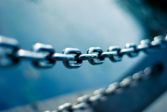 A close-up of a sturdy metal chain linking together against a blurred blue background, symbolizing a connected and resilient supply chain.