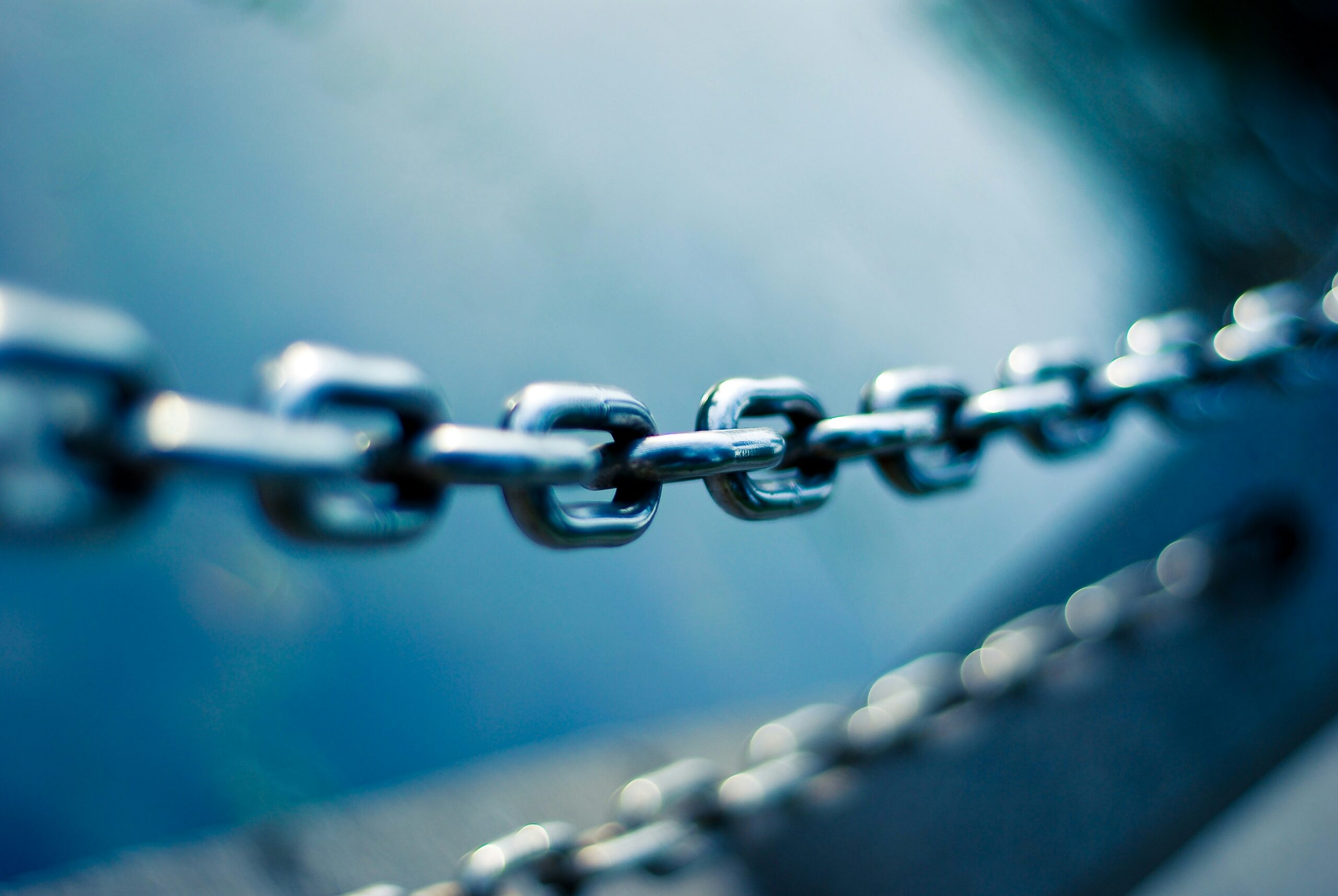 A close-up of a sturdy metal chain linking together against a blurred blue background, symbolizing a connected and resilient supply chain.