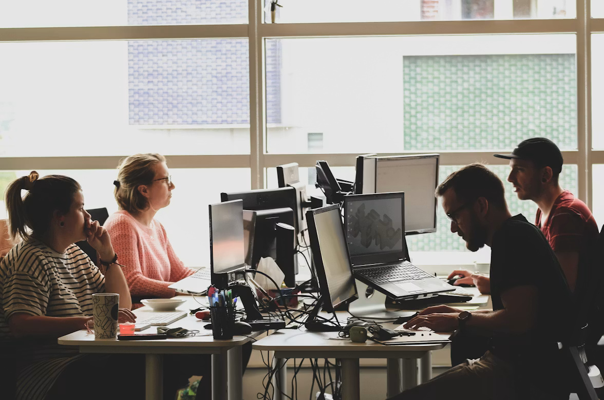 Four people working at their desks, illustrating what SAP security and development teams working at computers as they review patching, authentication, and software supply chain risks looks like.