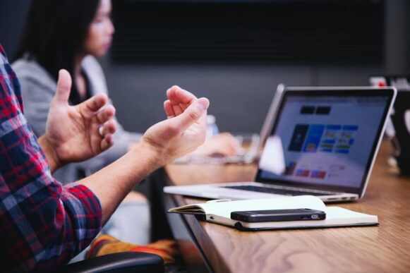 Person gestures during a meeting beside a laptop, illustrating SAP agentic AI for sales workflow planning.