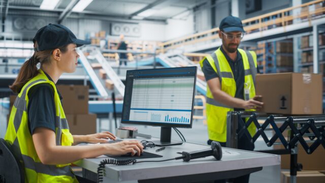Warehouse workers use inventory management software at a packing station in a distribution center.