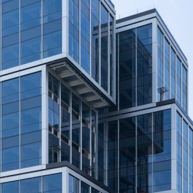 Modern glass office building facade with stacked cubic sections against a pale sky, representing the real estate and housing industry served by Aareon's SAP S/4HANA-based property management ERP