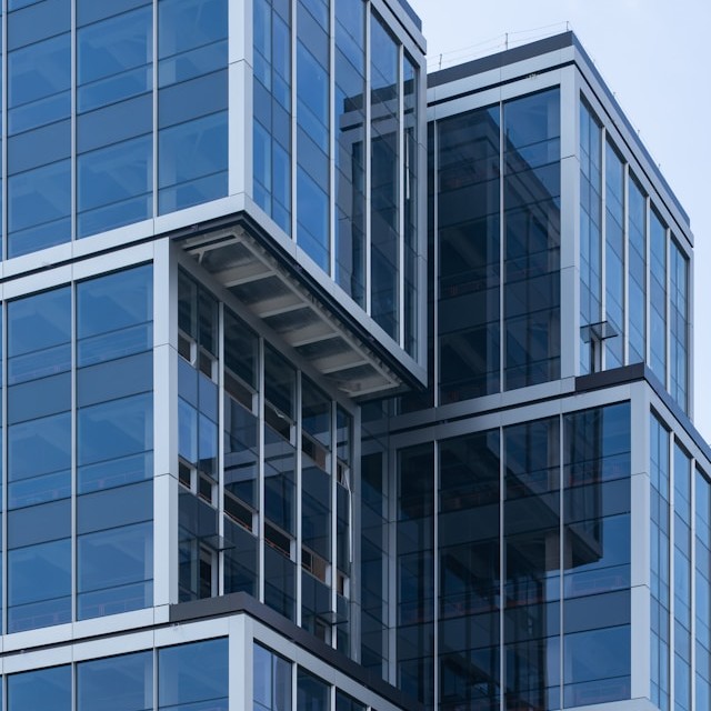 Modern glass office building facade with stacked cubic sections against a pale sky, representing the real estate and housing industry served by Aareon's SAP S/4HANA-based property management ERP