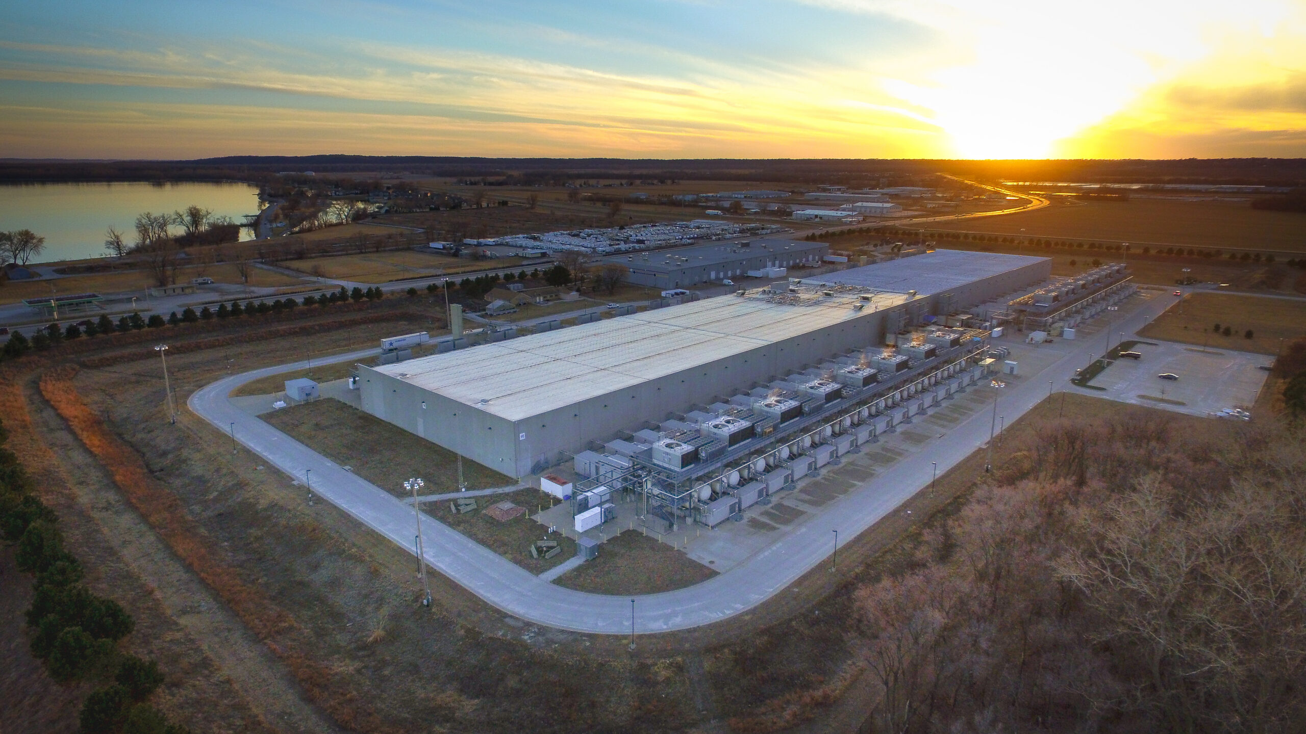 Aerial view of a large data center campus with cooling systems, service roads, and surrounding infrastructure.