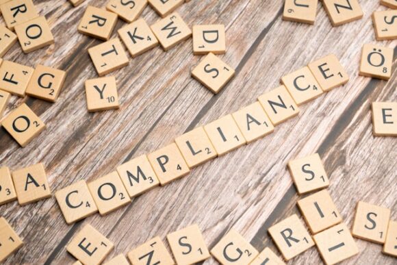 Wooden Scrabble tiles spelling the word "compliance" across a rustic wood surface, surrounded by scattered loose letter tiles, representing the SAP Segregation of Duties and access governance discipline ToggleNow argues must be built into every role assignment.