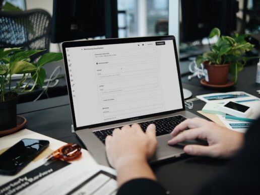 A professional working at a laptop displaying an SAP invoice-processing document-edit screen at a desk with paperwork and a smartphone, representing SAP Invoice Management by OpenText and SAP Information Capture extracting ESG data from utility invoices.