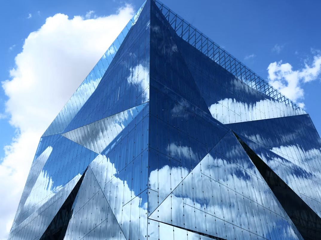 Clouds reflected across a modern glass office building, illustrating SAP Cloud ALM and complex enterprise operations.