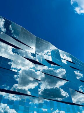 Modern office building with a mirrored glass facade reflecting white clouds and blue sky, representing SAP Cloud ERP security and the shared responsibility model in cloud migration