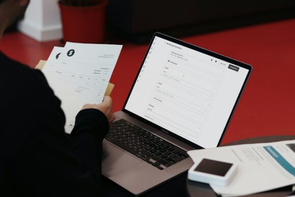Finance professional holding paper invoices while reviewing a digital billing form on a laptop, illustrating invoice processing and billing cycle time in SAP finance operations