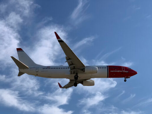 Norwegian Air Shuttle aircraft landing at Málaga Airport under a blue sky.