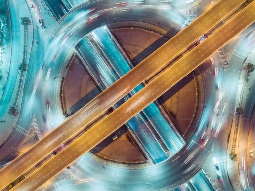Aerial view of a multilevel highway interchange at night, with light trails flowing between connected roads, illustrating process orchestration