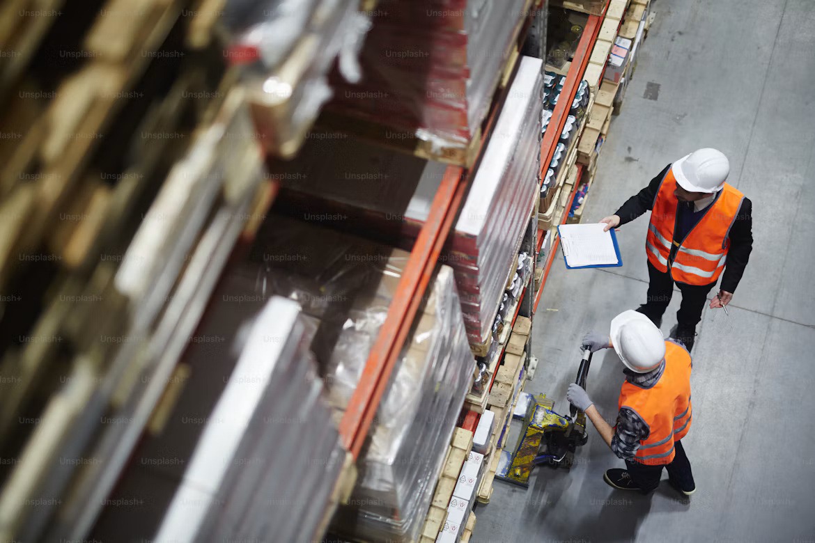 Warehouse workers review inventory beside stacked pallets, illustrating the operational complexity behind pricing, rebates, and margin visibility.