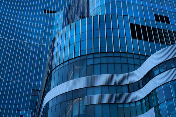 Close-up of a modern building's blue glass facade, featuring curved architectural elements and repeating geometric patterns.