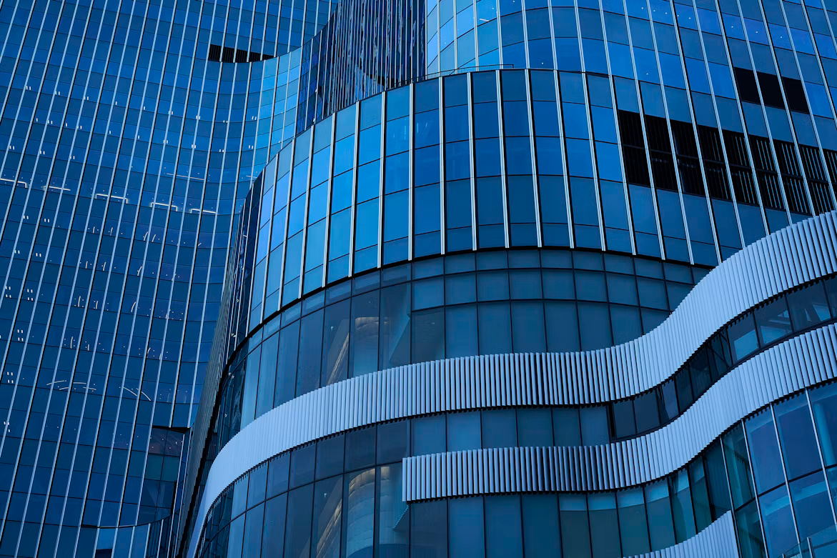 Close-up of a modern building's blue glass facade, featuring curved architectural elements and repeating geometric patterns.