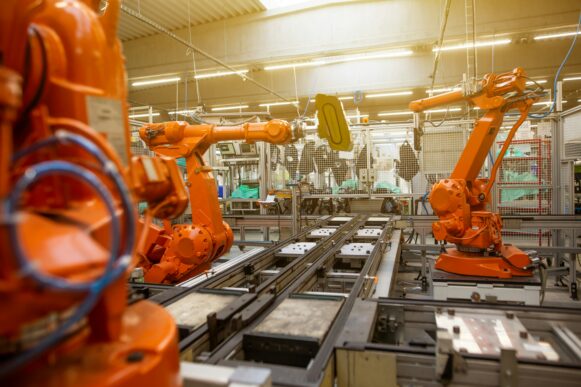 Orange industrial robotic arms positioned around an automated production line inside a manufacturing facility.