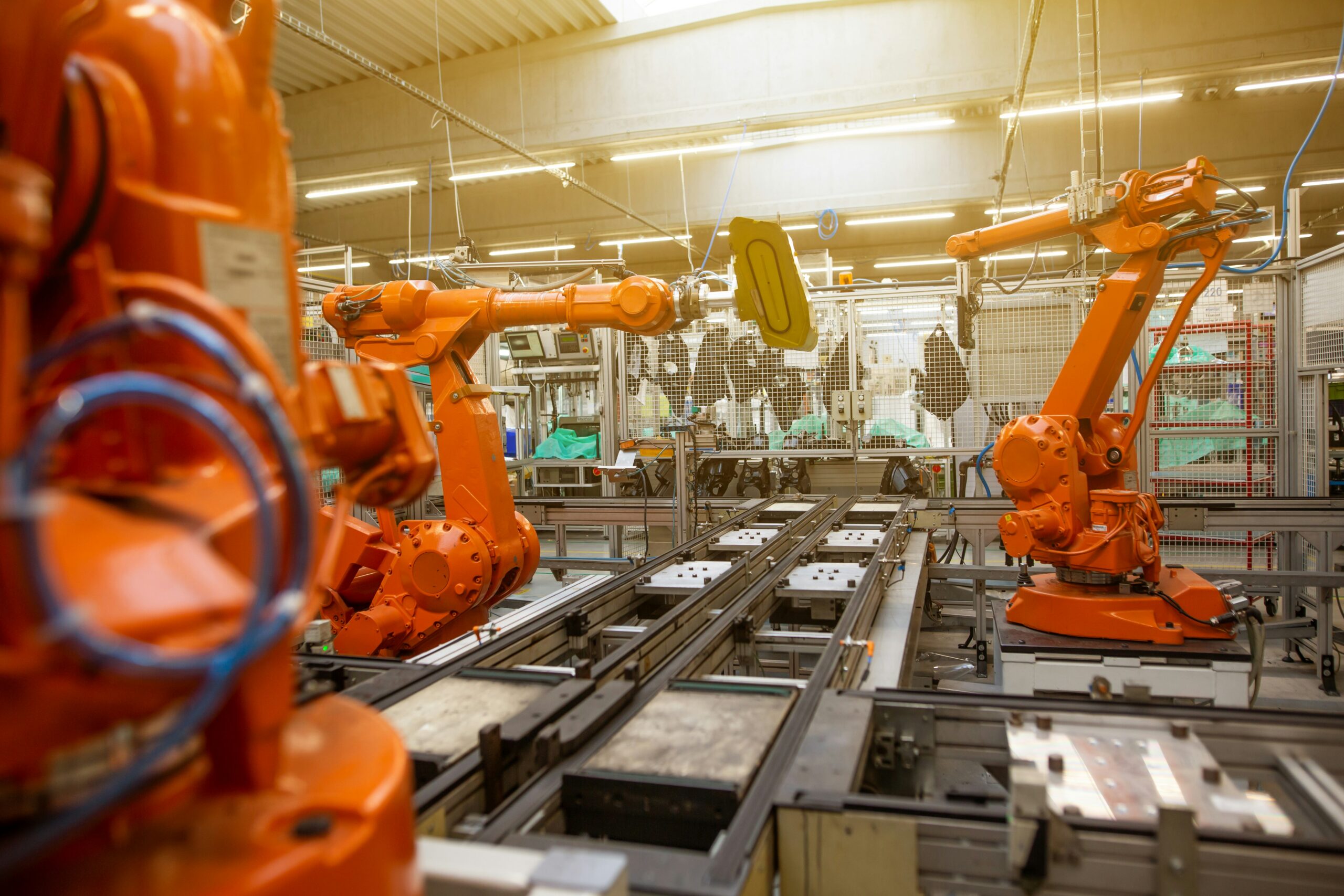 Orange industrial robotic arms positioned around an automated production line inside a manufacturing facility.